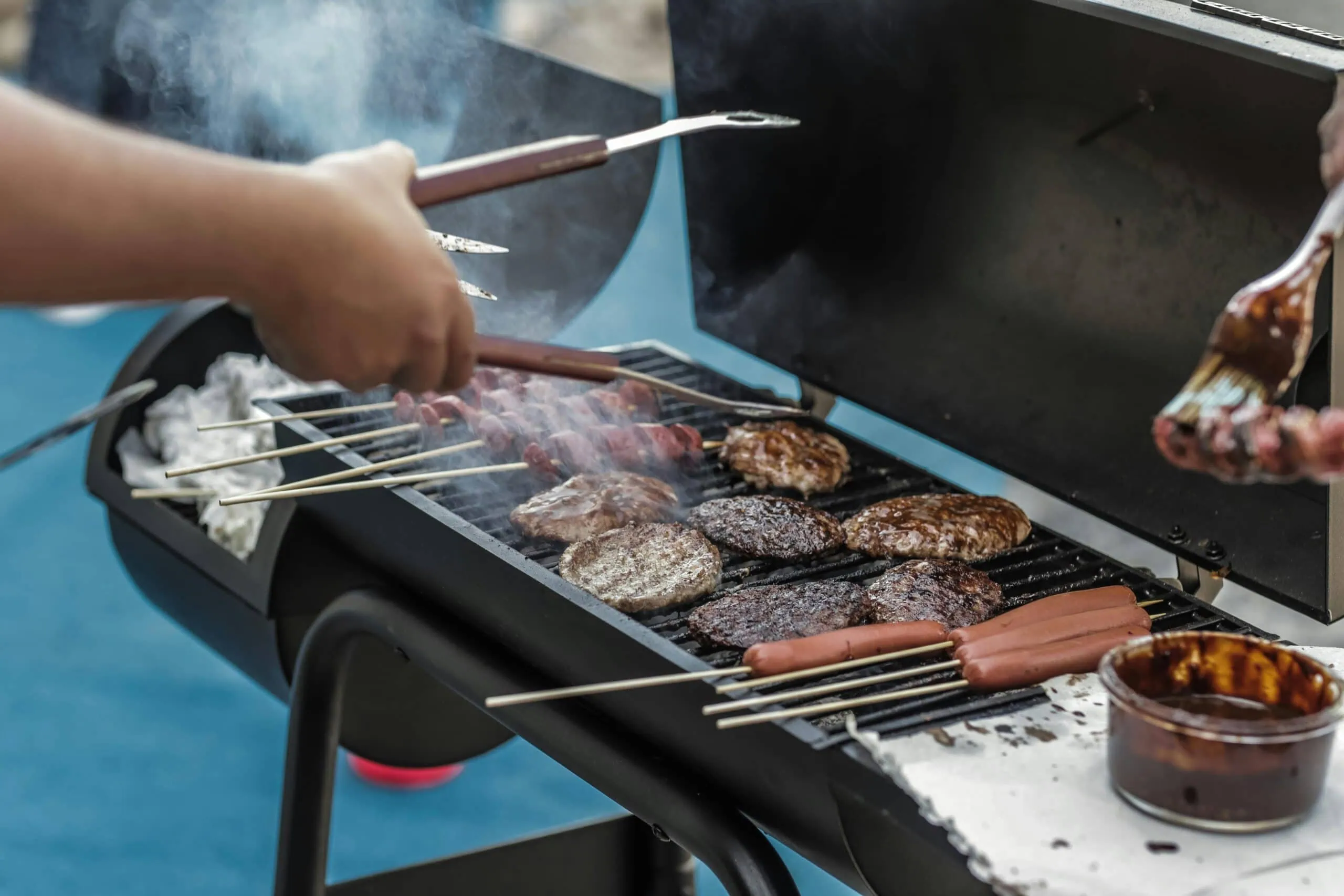 Delicious meats and sausages grilling on a barbecue outside, perfect for a summer picnic.