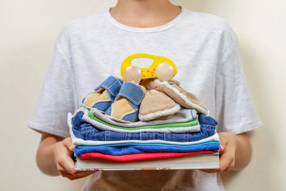 Soft cloth baby clothes and toy with stack of books in person holding hands, for prenatal and baby shower planning.project