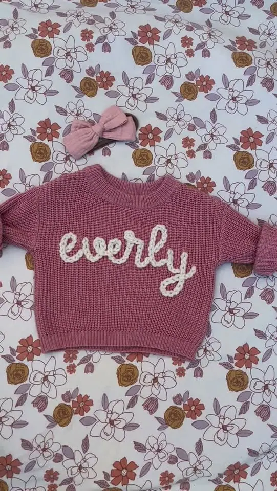 Baby sweater with "everly" embroidery and pink bow.