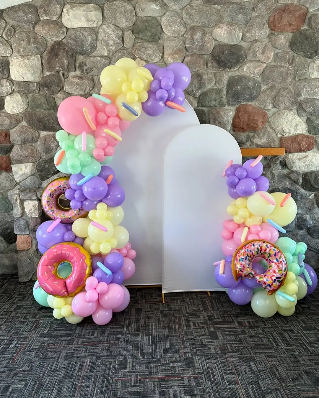 Balloon arch with pastel balloons and donut decorations for a baby shower.