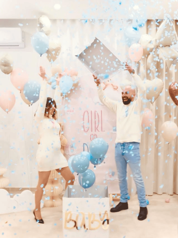 Happy couple celebrating gender reveal with balloons and confetti at baby shower.