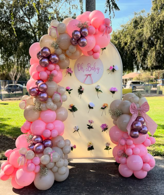Colorful pink and pearl balloon arch with floral accents for a baby shower backdrop.