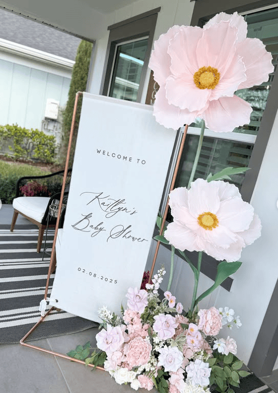 Beautiful pink and white floral baby shower welcome sign with large paper flowers.