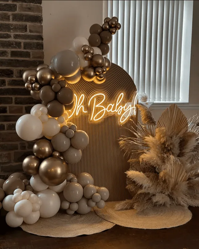 Elegant balloon arrangement with neon "Oh Baby" sign for boho baby shower.