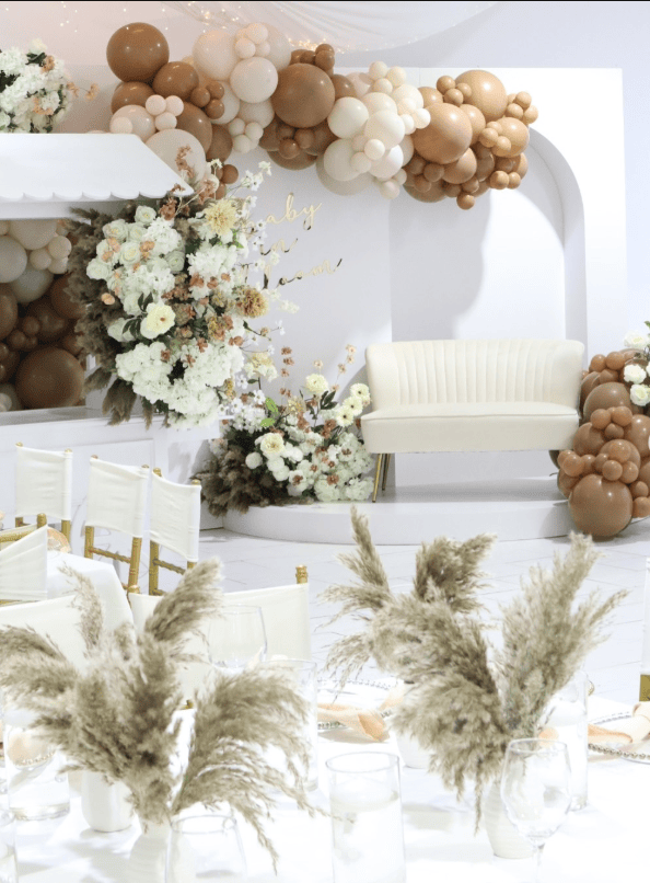 Beautiful boho-themed baby shower setup featuring balloon arch, floral arrangements, and cozy seatin.
