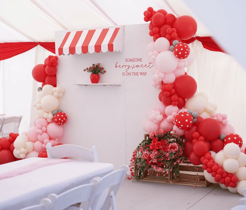 Balloon arch with red, pink, and white balloons for a strawberry-themed baby shower.