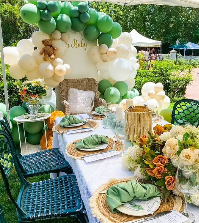 Elegant garden baby shower setup with balloon arch, floral centerpieces, and outdoor seating.