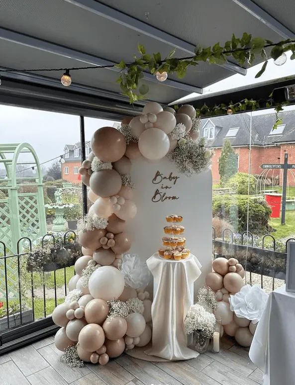 Elegant balloon arch with neutral tones and floral accents for spring baby shower celebration.