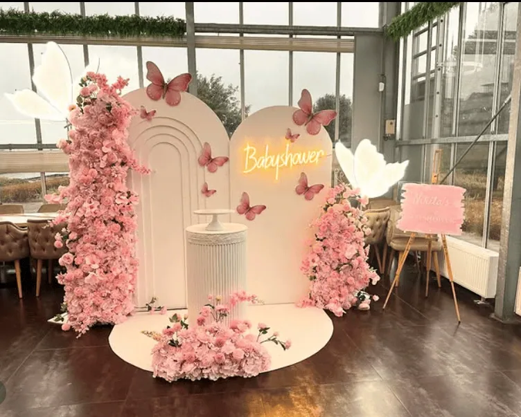 Elegant pink floral baby shower backdrop with butterflies and soft lighting.