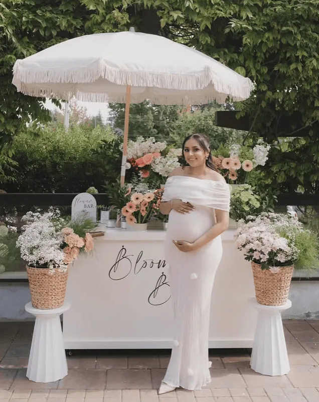 Pregnant woman at a baby shower with floral decorations and white umbrella.