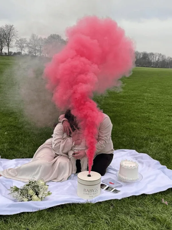 Couple sharing a gender reveal moment with pink smoke explosion outdoors.
