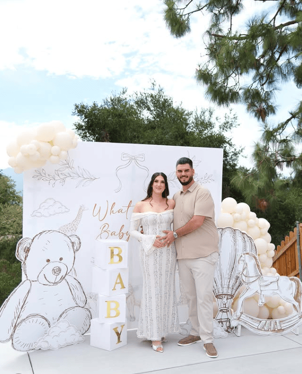 Cute couple at gender reveal party with teddy bear and balloon decor.