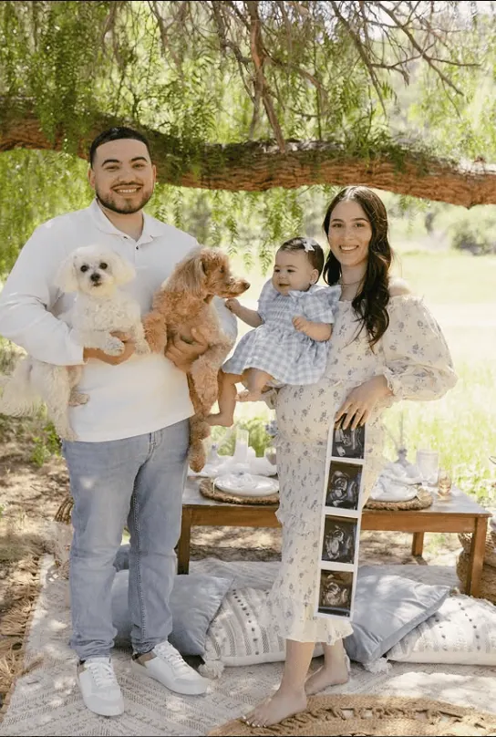 Happy family celebrating gender reveal outdoors with pets and ultrasound photos.