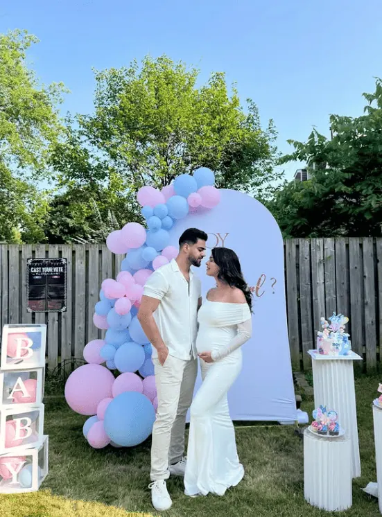 Cute couple at gender reveal party with pastel balloons and decorations.