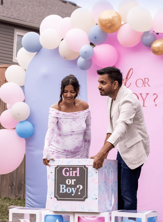 Happy couple at gender reveal party with balloons and a box labeled "Girl or Boy?".