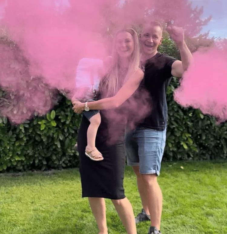 Happy family holding daughter with pink smoke for gender reveal celebration.