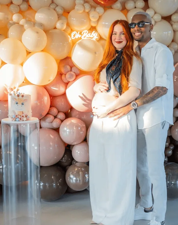 Happy couple at gender reveal party with balloon backdrop and "Oh Baby" sign.