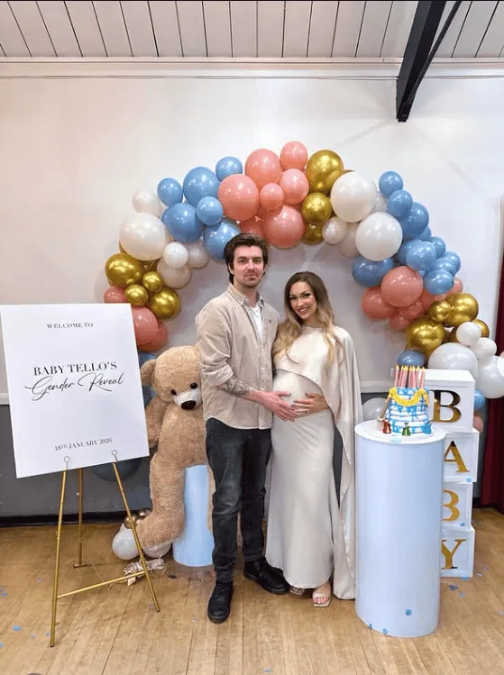 Pregnant woman and partner at gender reveal party with balloons and cake.
