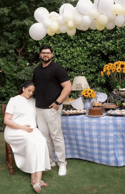 Expecting couple at gender reveal party with balloons and dessert table.