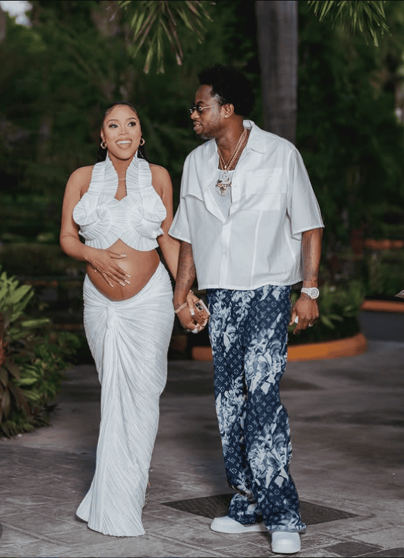 Pregnant woman and partner holding hands outdoors during gender reveal celebration.