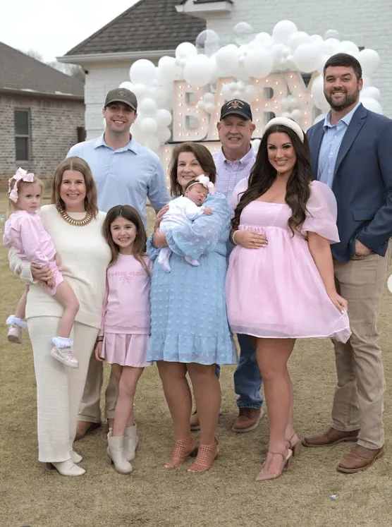 Family celebrating a gender reveal party outdoors with balloons and happy faces.
