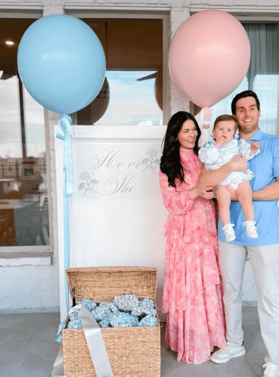 Happy family holding baby girl with pink and blue balloons.