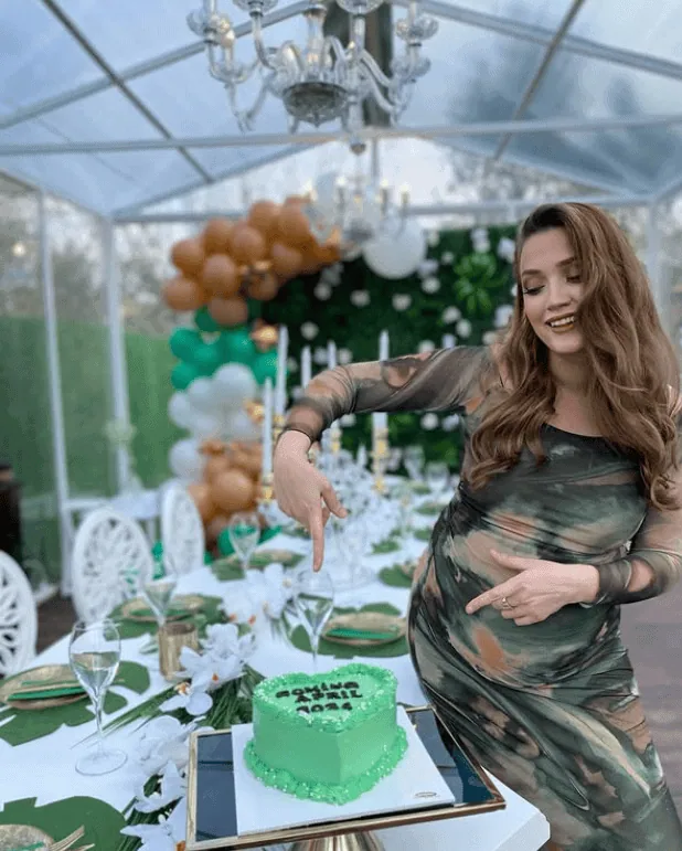 Pregnant woman celebrating baby shower with cake and decorations.