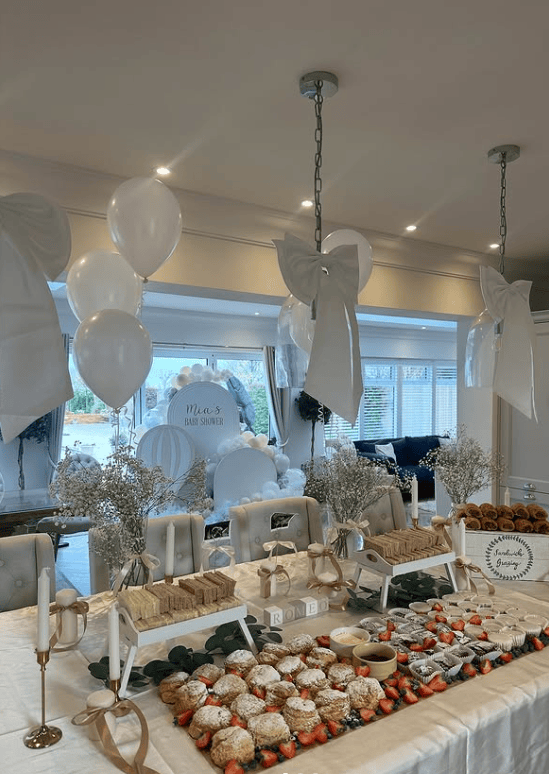 Elegant baby shower dessert table with cupcakes, cookies, and balloons.