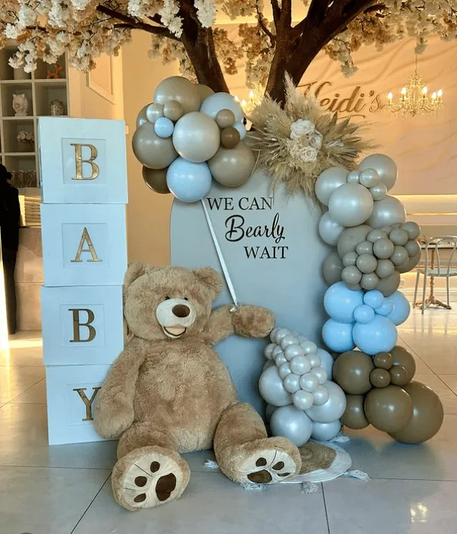 Baby shower balloon arrangement with teddy bear, floral accents, and "We Can Bearly Wait" sign.