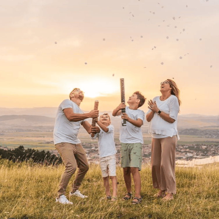 Family enjoying a gender reveal with confetti and party poppers outdoors.