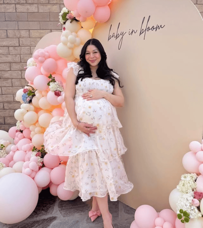 Pregnant woman at baby shower with pink and white balloons and floral accents.