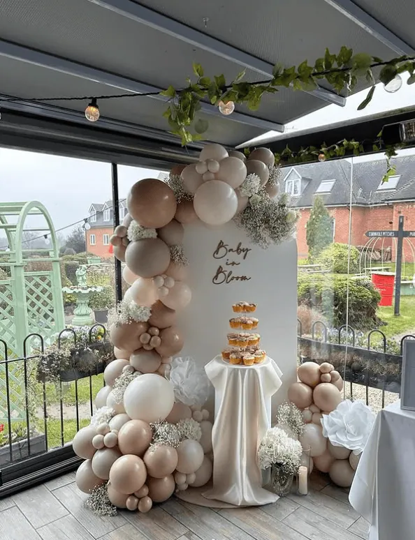 Elegant balloon arch with neutral tones and floral accents for a baby shower celebration.
