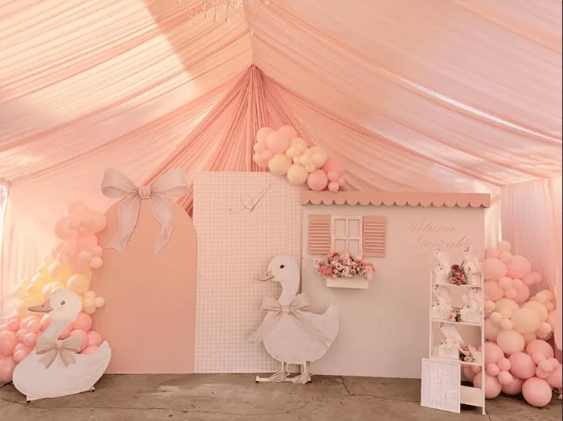 Elegant pink and white vintage baby shower setup with swan and balloon decorations.