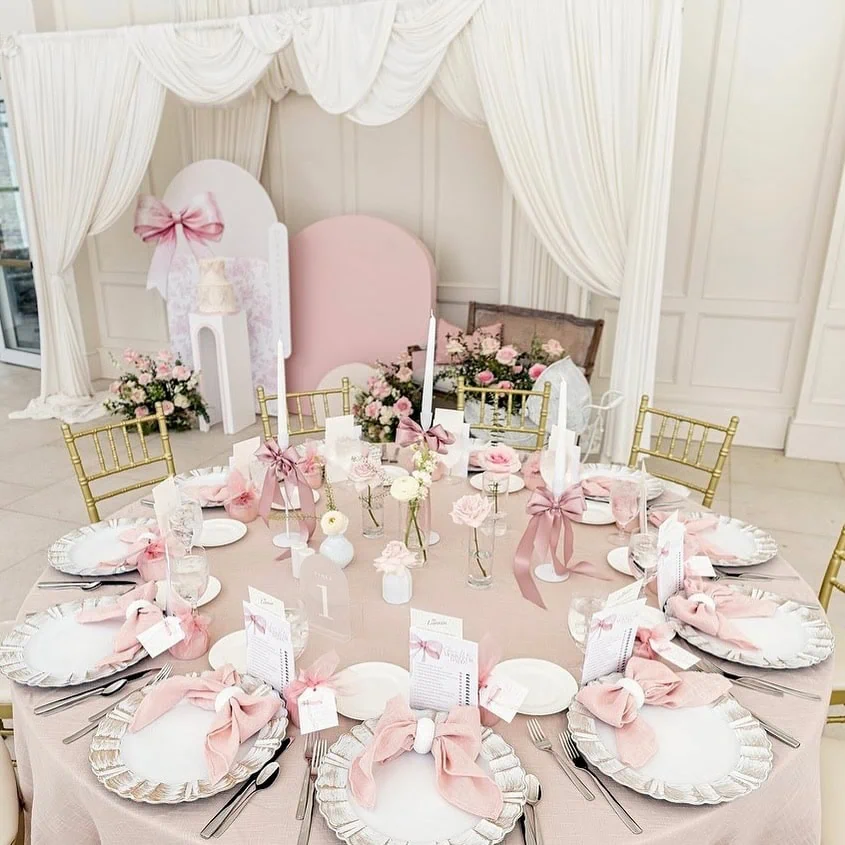 Elegant baby shower table with pink, white, and gold accents, floral arrangements, and themed decora.