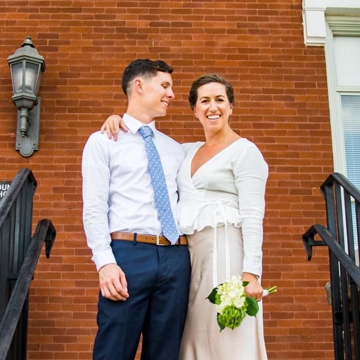 Smiling couple at baby shower outside house with brick wall and stairs.