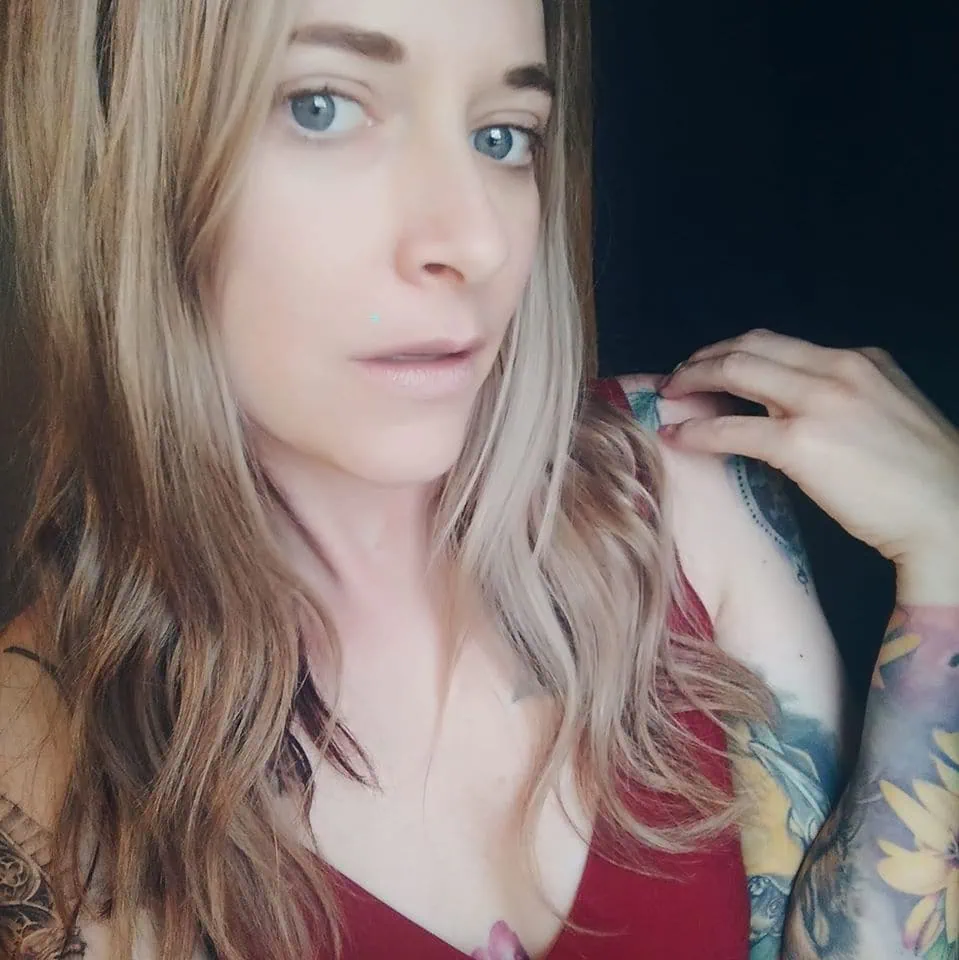 Portrait of a woman with tattoos, blue eyes, and wavy hair.