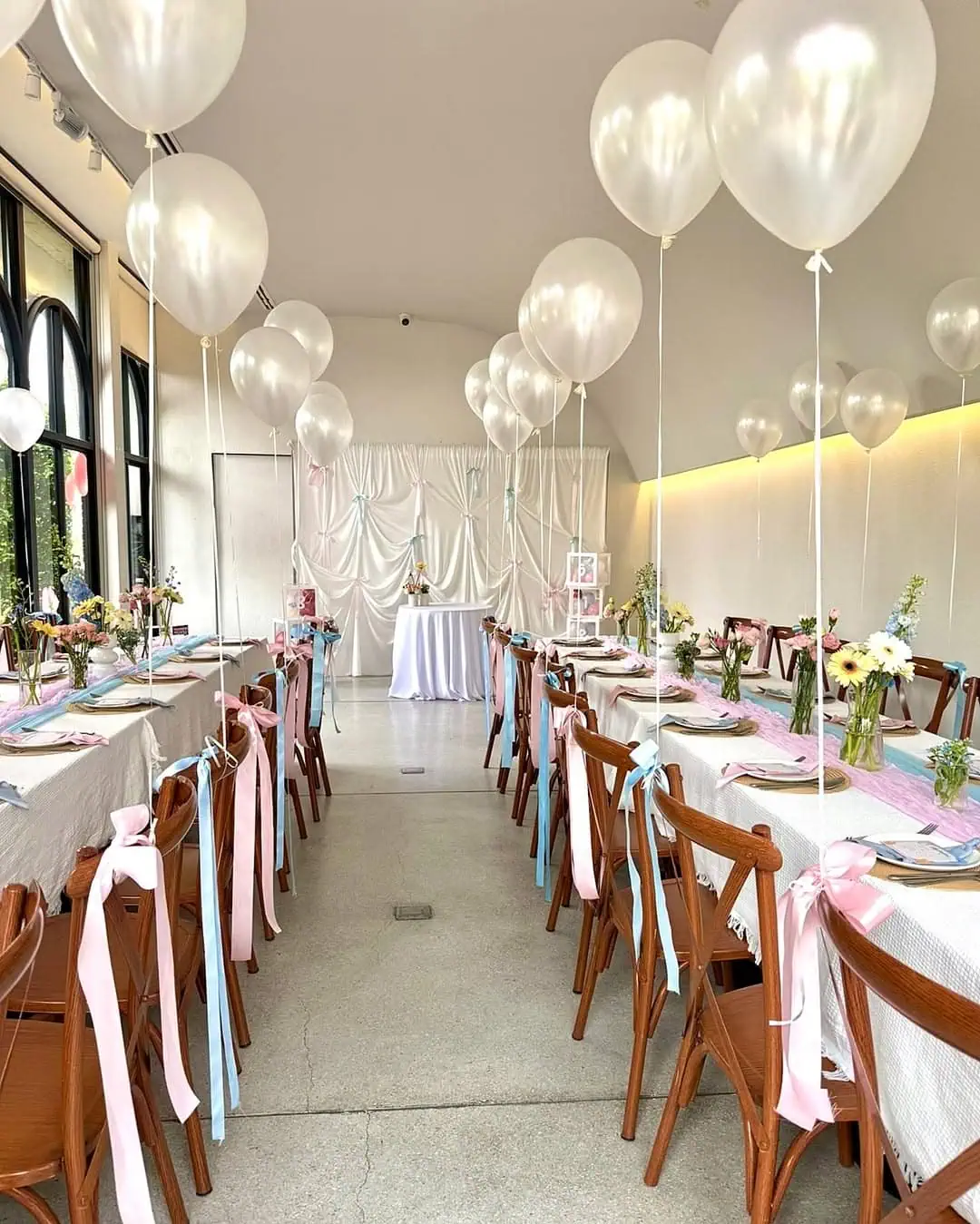 Decorated baby shower tables with pink ribbons, white balloons, and floral centerpieces.