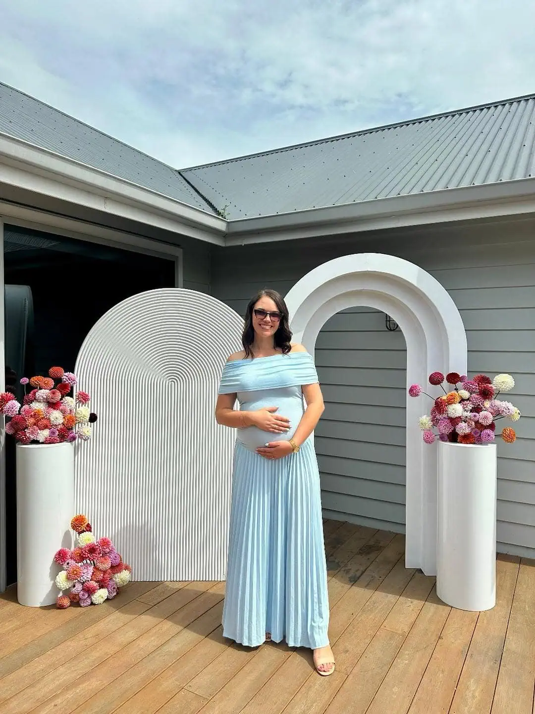 Pregnant woman in blue dress at outdoor baby shower with floral decorations.