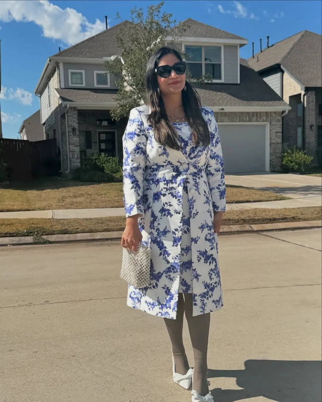 Pregnant woman in floral dress with sunglasses and handbag outside.