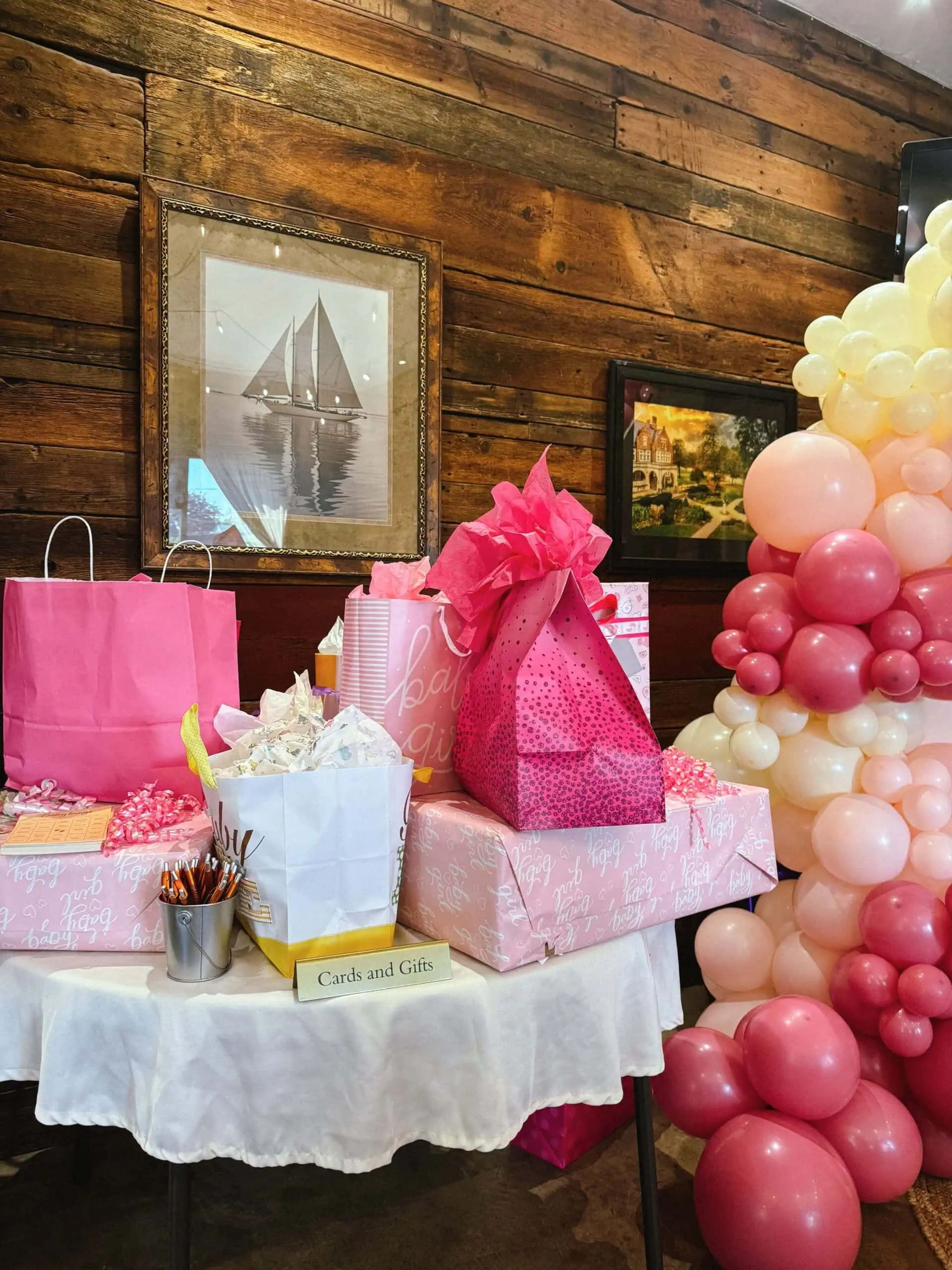 Decorative baby shower gift table with pink and white balloons and presents.