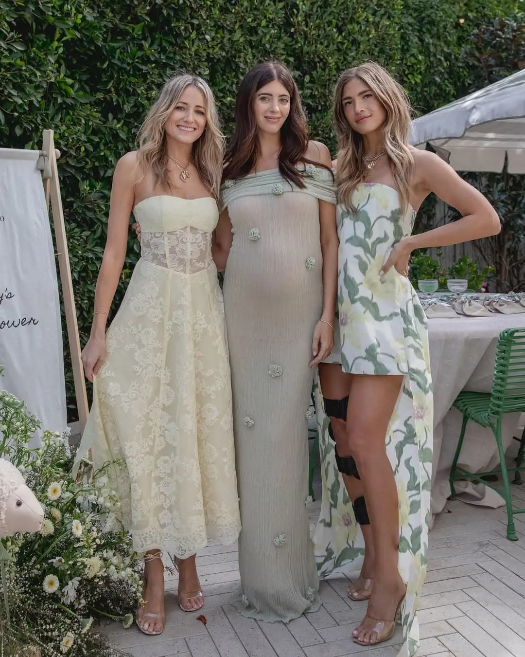 Three women in elegant summer dresses at outdoor baby shower event.