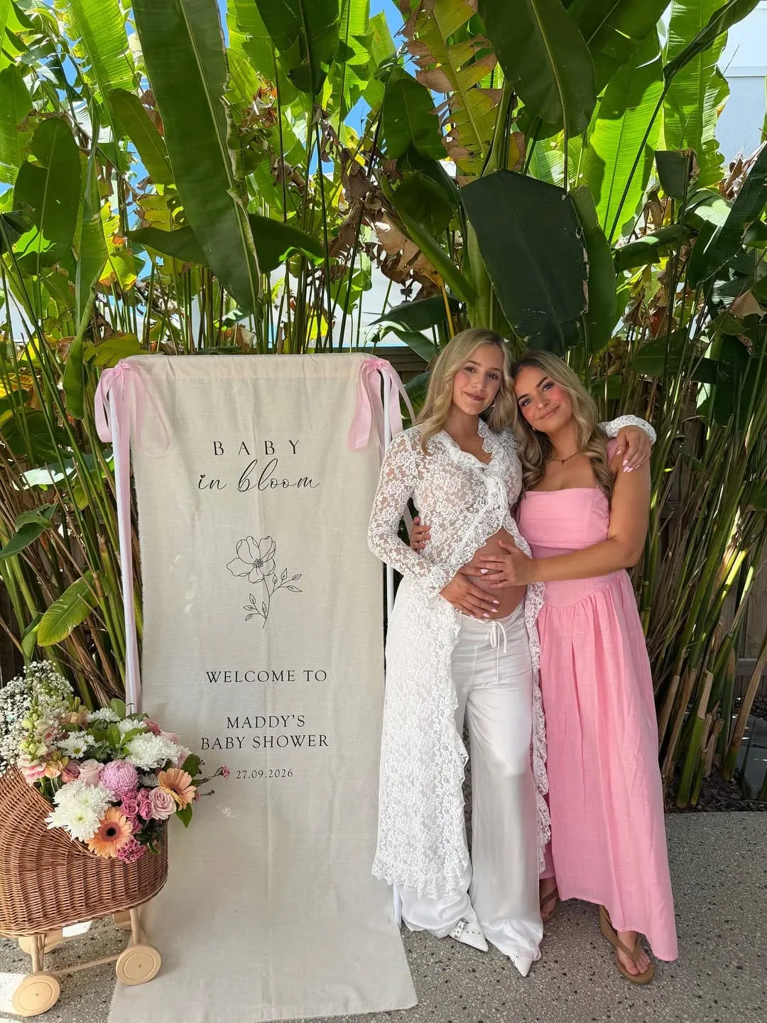 Two pregnant women at a baby shower with tropical plants and floral decor.